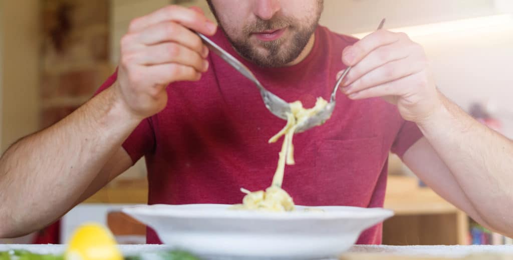 Young man eating pasta with a fork and spoon